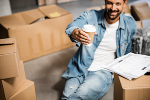 Happy attractive man with hot drink in new flat